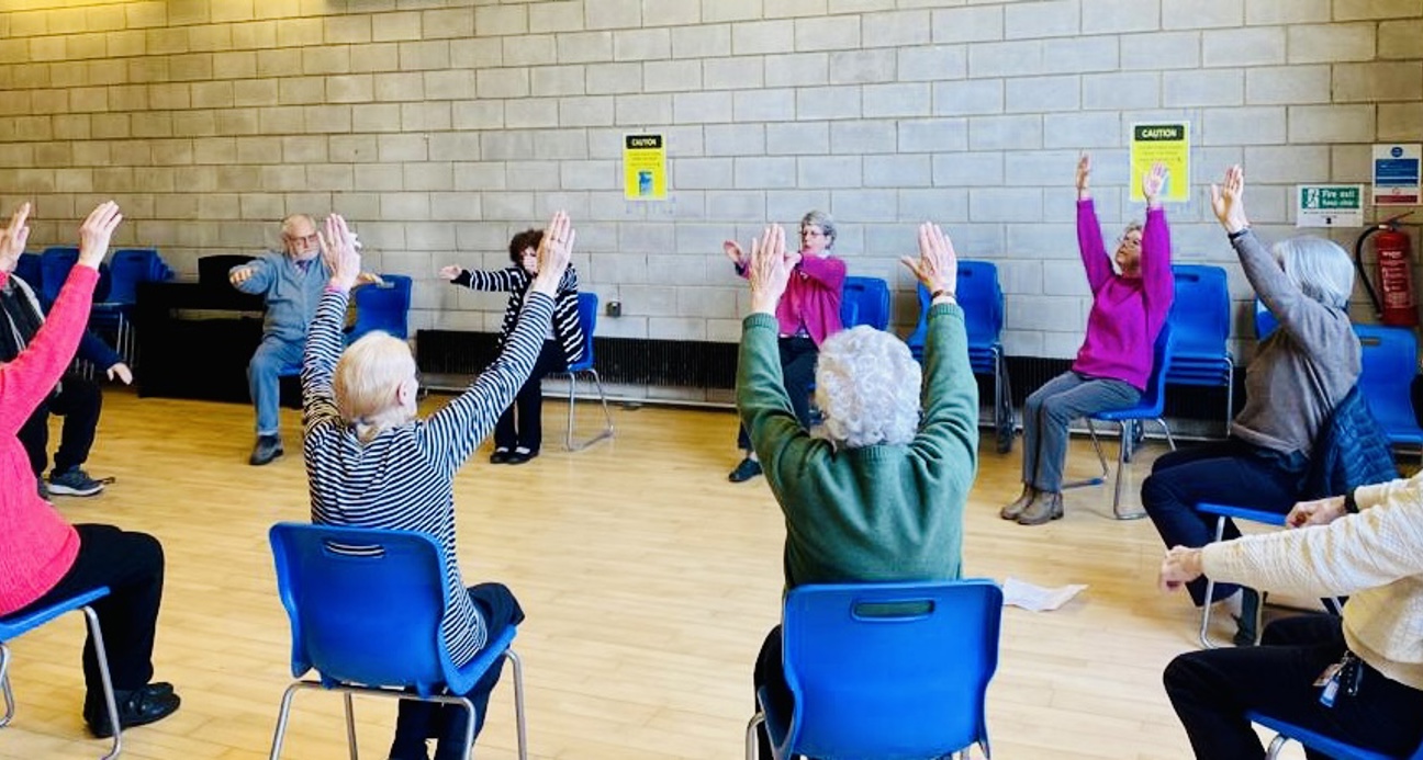 Group of older people sitting in a circle taking part in chair exercises