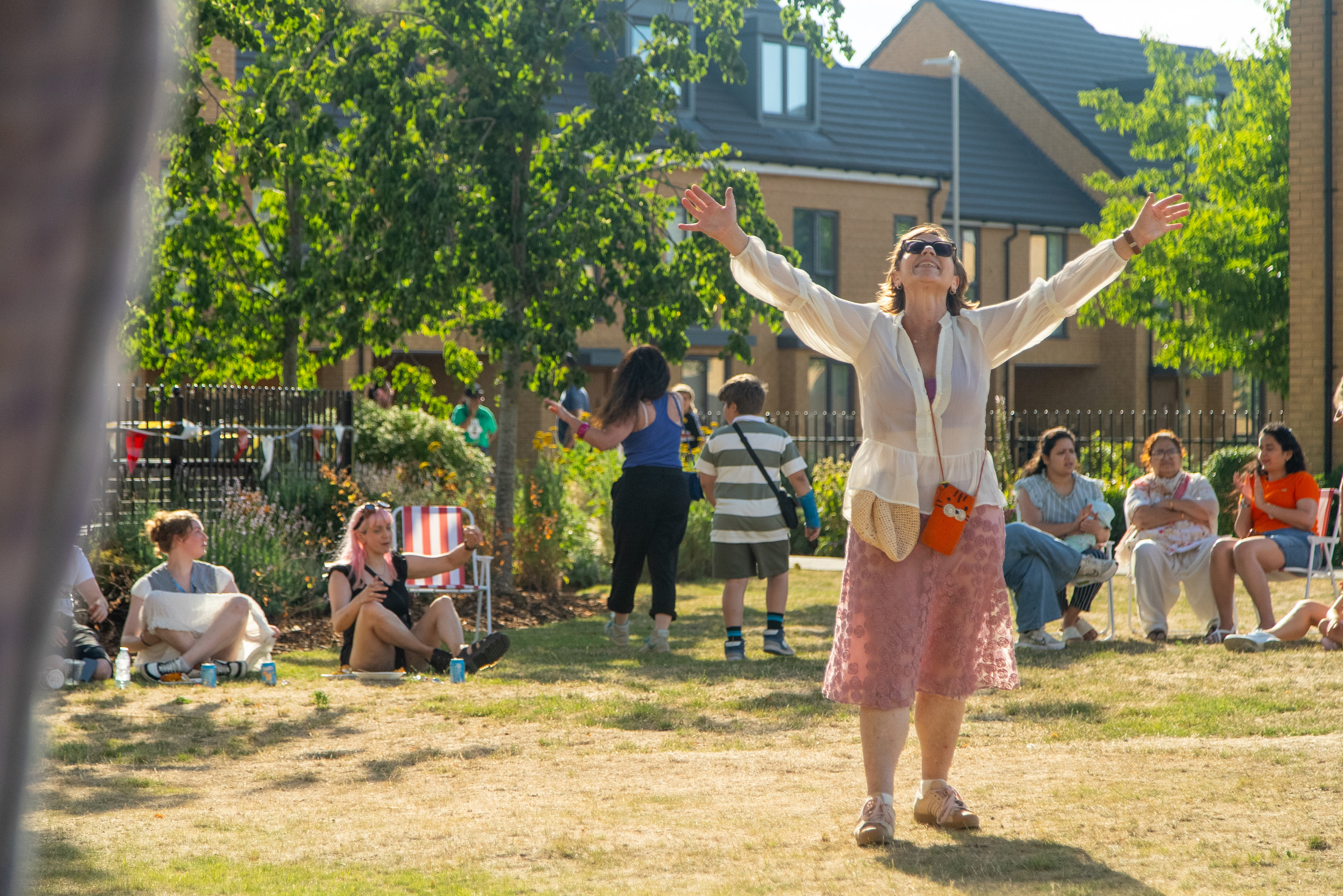 Woman reaching upwards in a green space surrounded by people and a housing estate