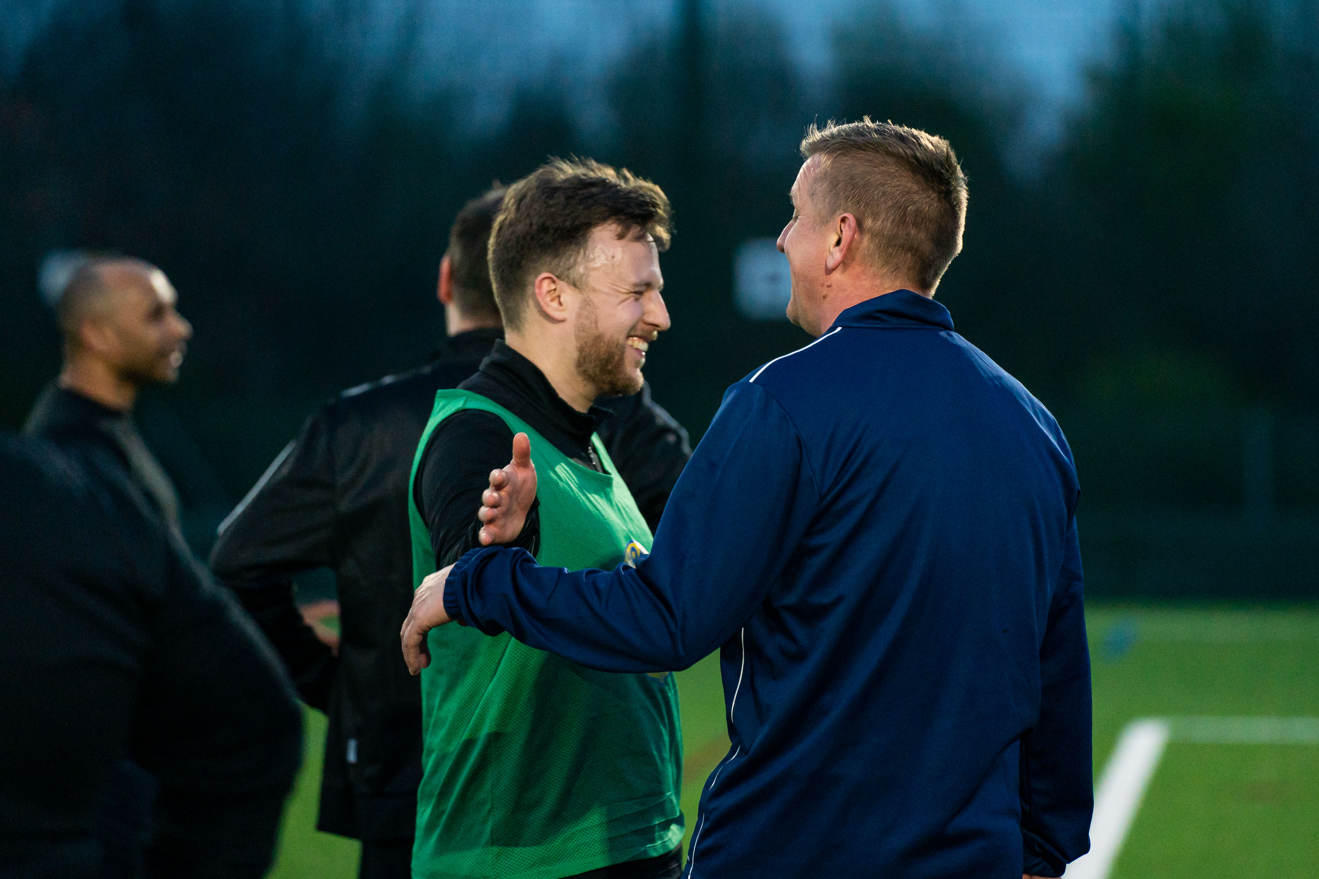 Two men on a football pitch laughing