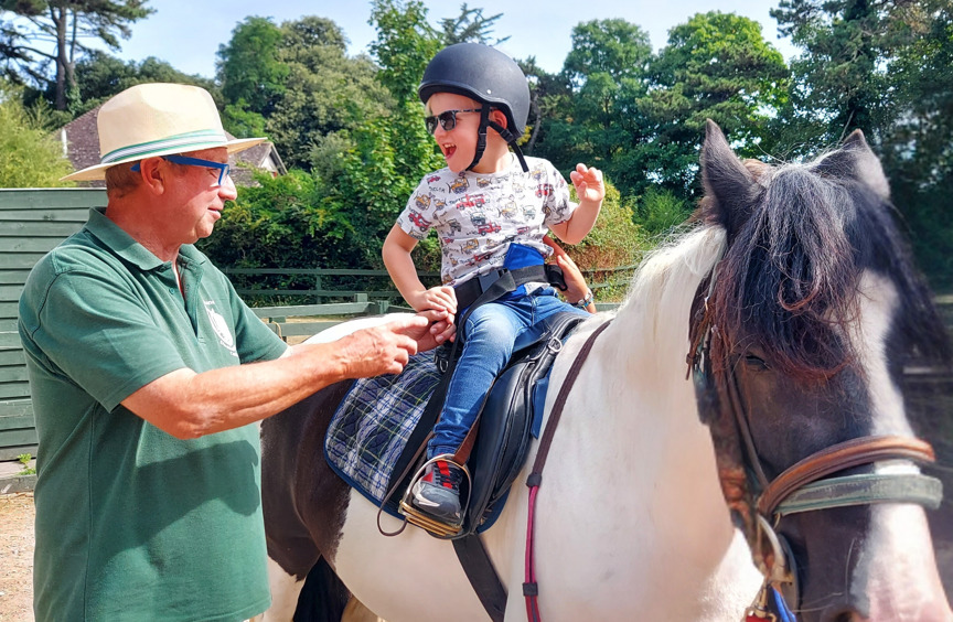Young child sitting on a horse with adult standing beside him
